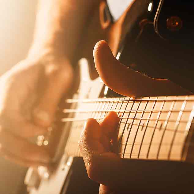 A rocker playing the electronic guitar at a concert on the stage with mist and light.