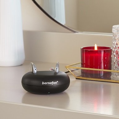 Bernafon Alpha rechargeable hearing aids in robust charger on a beauty table with mirror and a vase of dry flowers