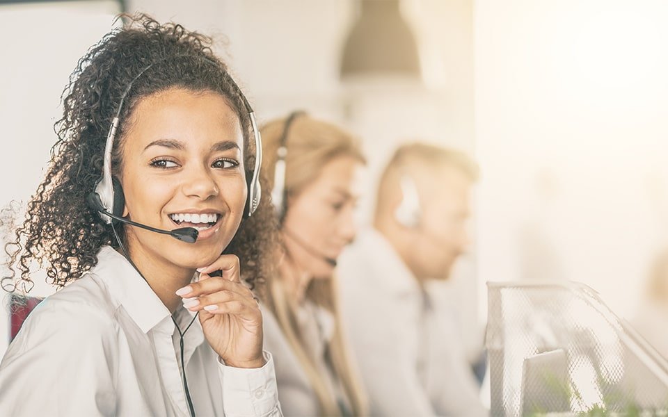 Smiling woman wearing headphones sitting next to two customer support colleagues