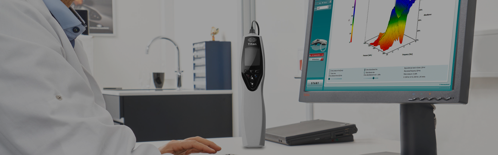 The Interacoustics Titan standing on a table, a doctor in from of a screen displaying WBT